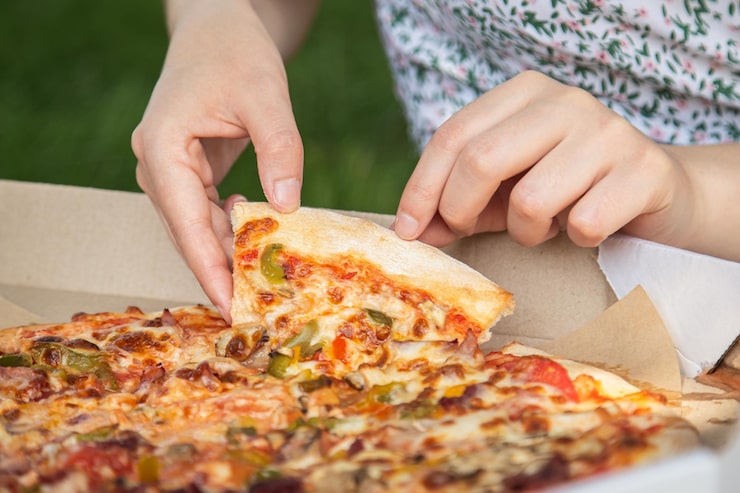 Manos tomando una porción de pizza desde la caja de delivery