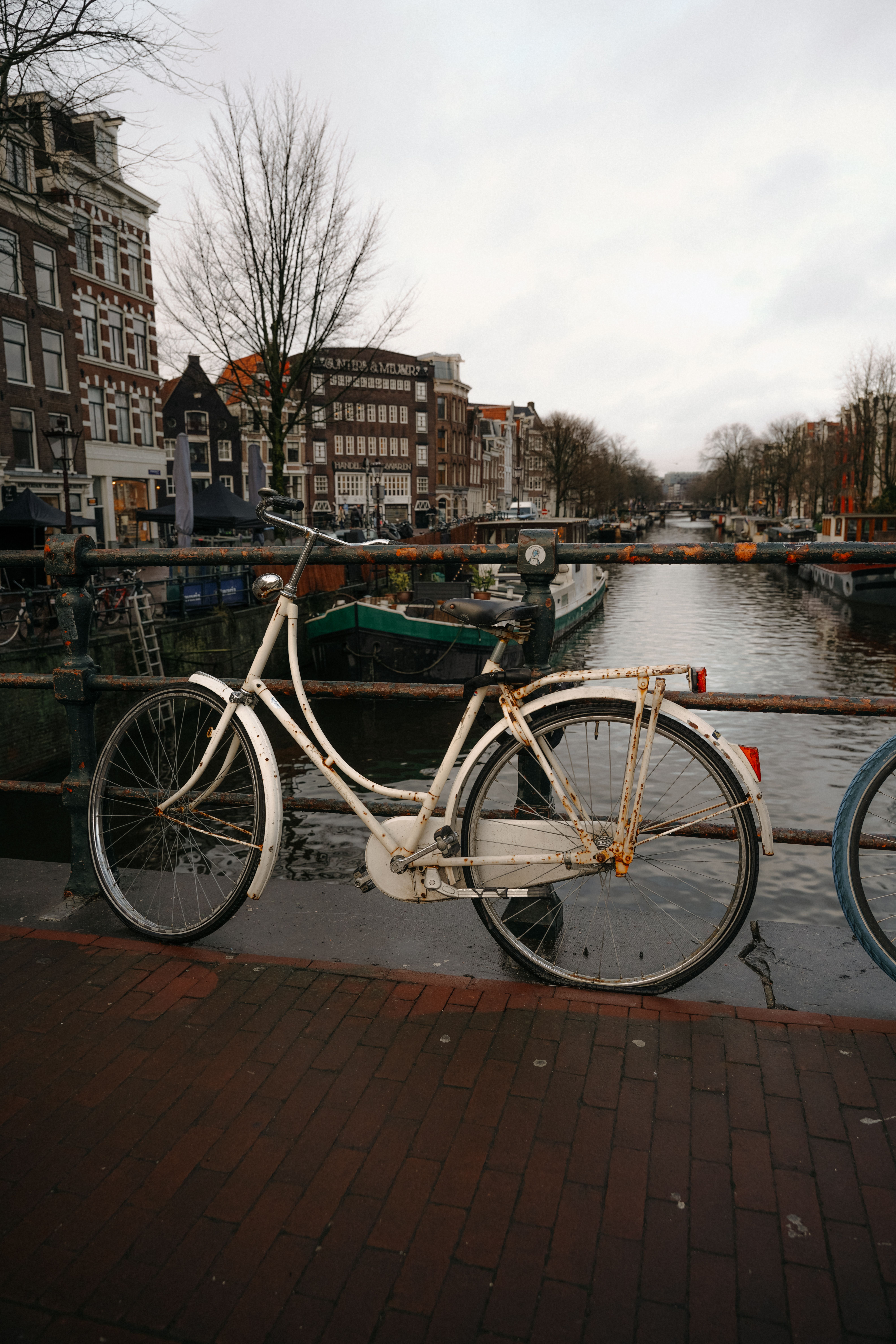A city bike locked to a canal bridge railing in Amsterdam; many newcomers rent from e-bike shops for internationals for a few weeks before committing to a purchase