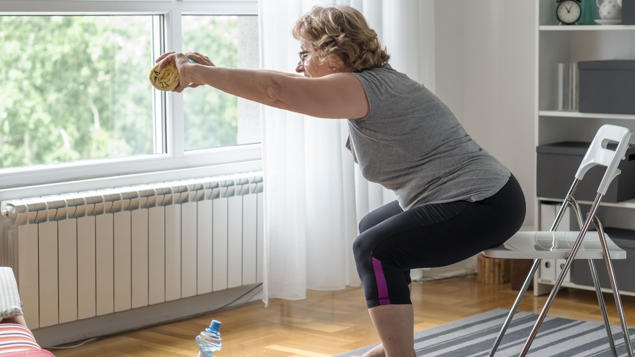 Senior woman performing a bodyweight arm exercise at home using a chair for support