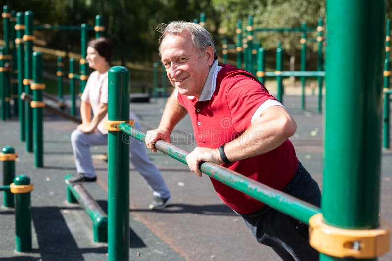 Older man doing incline push-ups using outdoor parallel bars at a fitness park