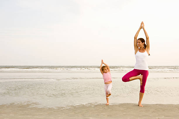Mother and child performing Vrikshasana Tree Pose together on beach