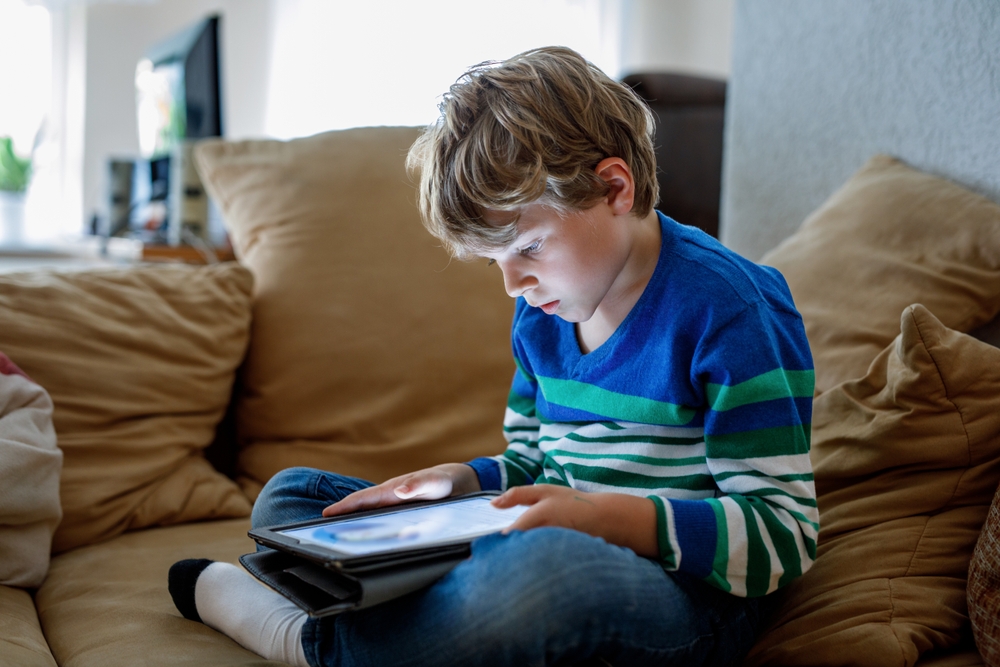 Child hunched over tablet on sofa with poor posture showing excessive screen time
