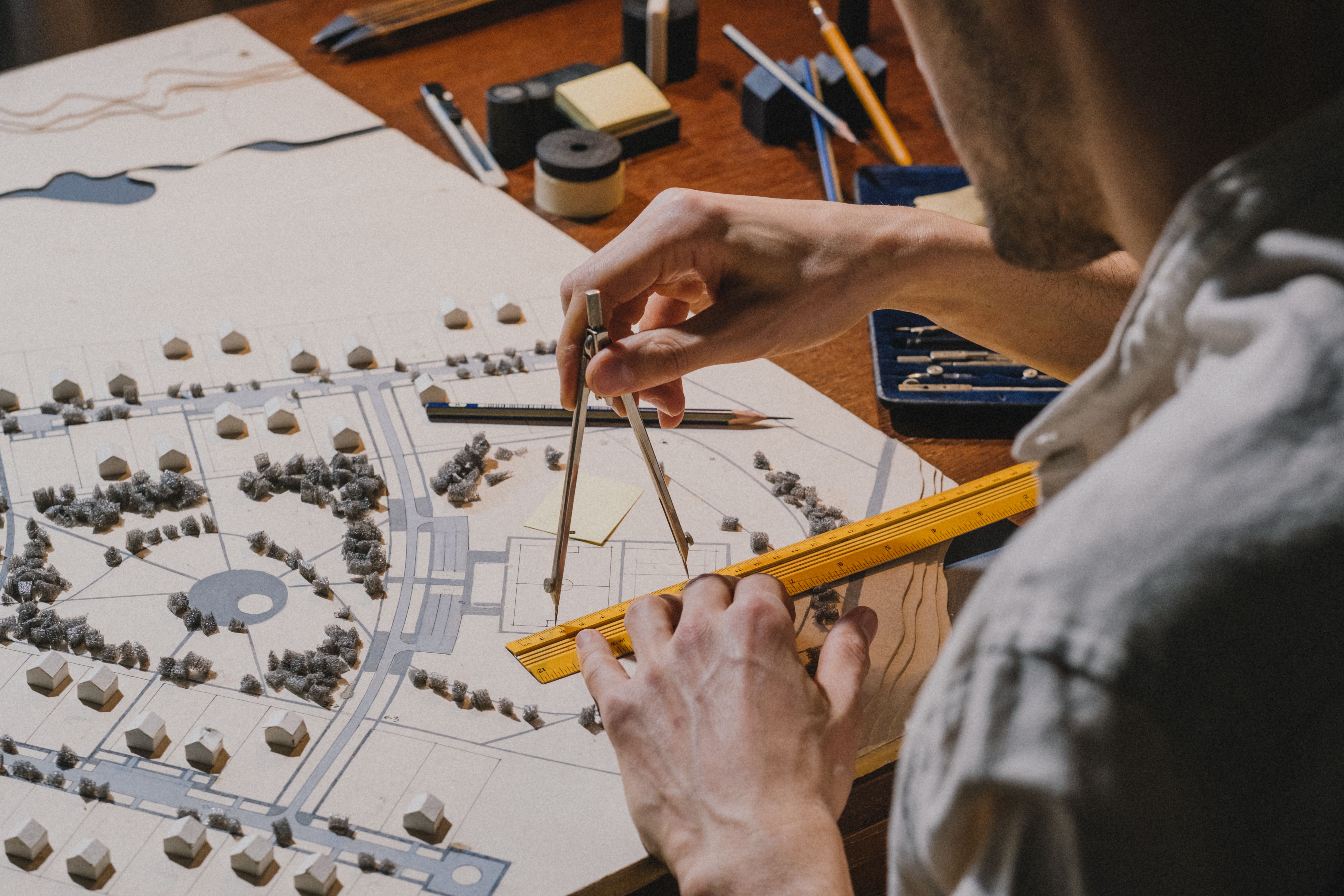 Architect's hands drafting over a detailed neighborhood model with compass and ruler