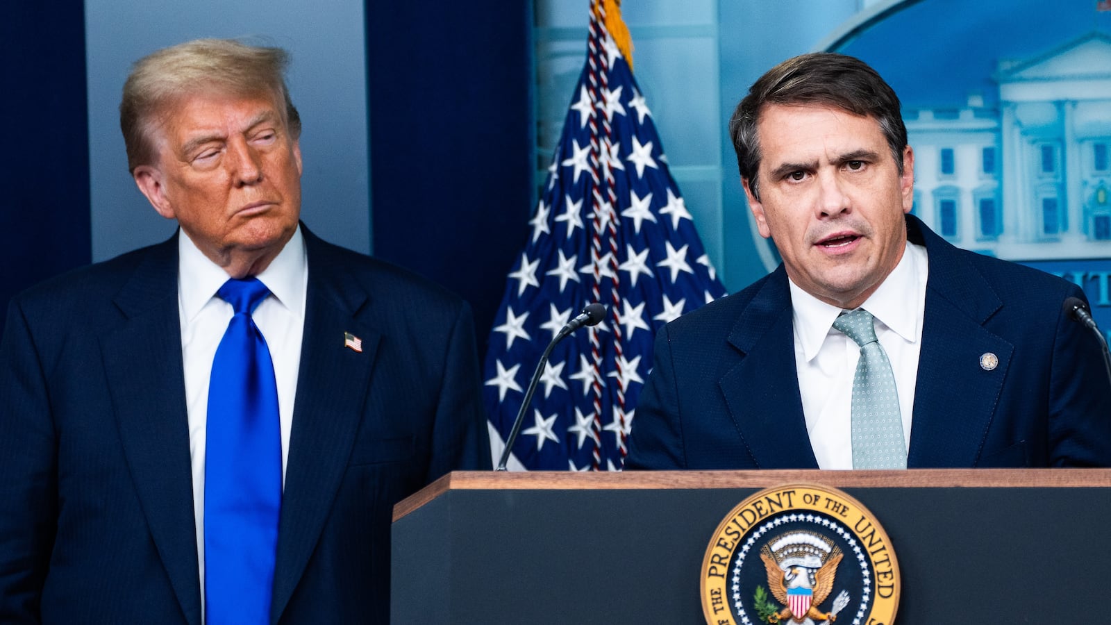 Donald Trump standing beside Todd Blanche at a podium with the presidential seal and an American flag