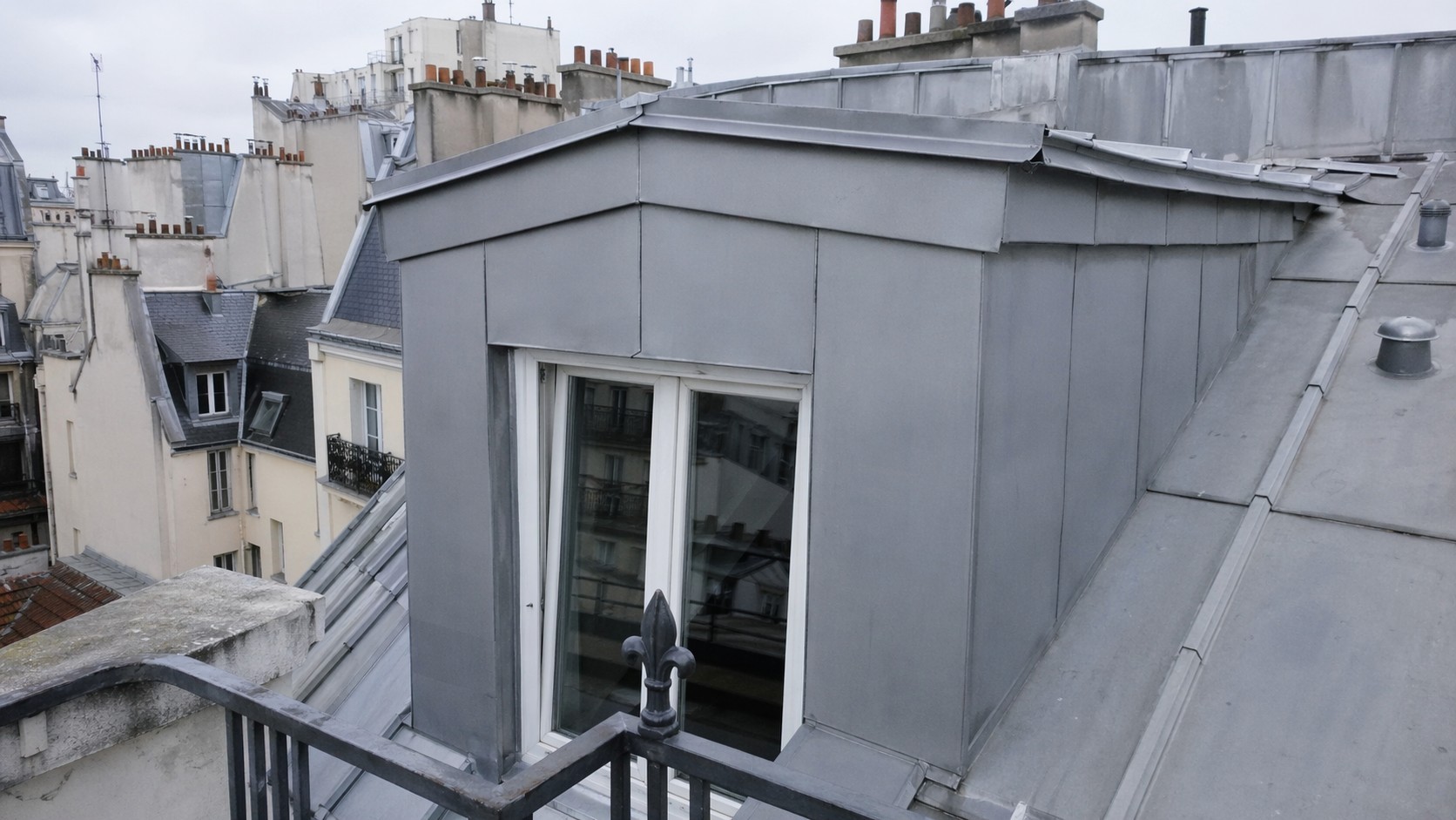 Photographie d'illustration : lucarne et entourages habillés de zinc sur une toiture de ville.