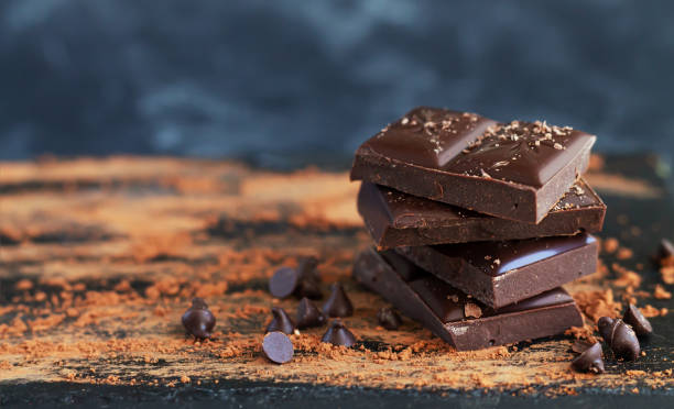 Stack of broken dark chocolate squares dusted with cocoa powder and chocolate chips on a dark rustic wooden board