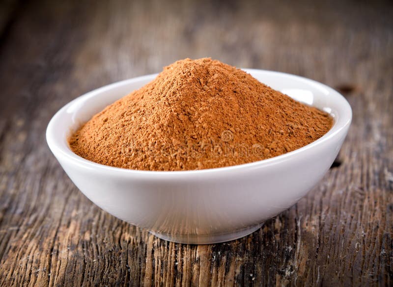 Ground Ceylon cinnamon powder mounded in a white ceramic bowl on a rustic dark wooden table