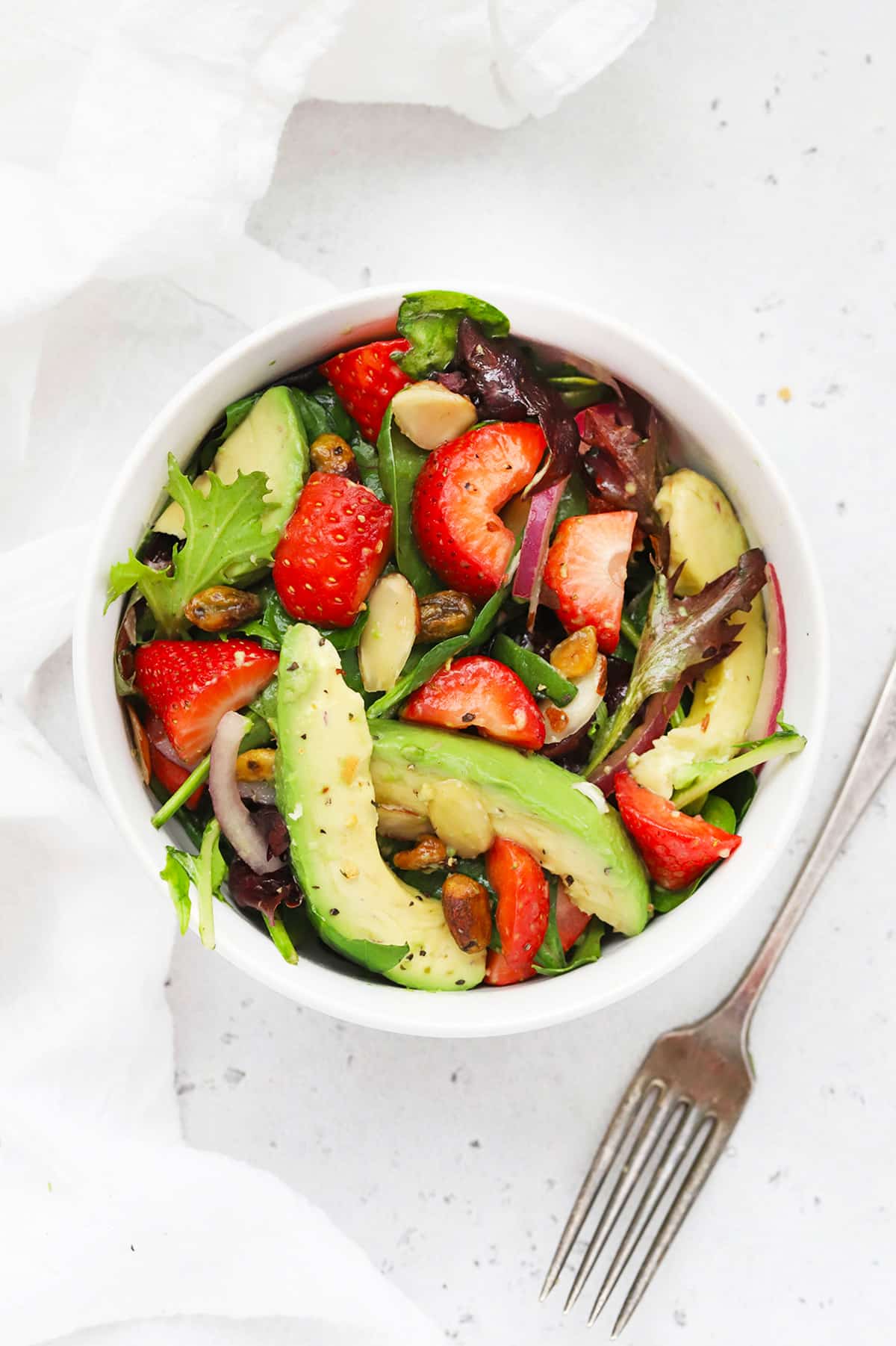 Fresh spinach salad bowl with sliced strawberries, creamy avocado, sliced almonds and red onion on a white background