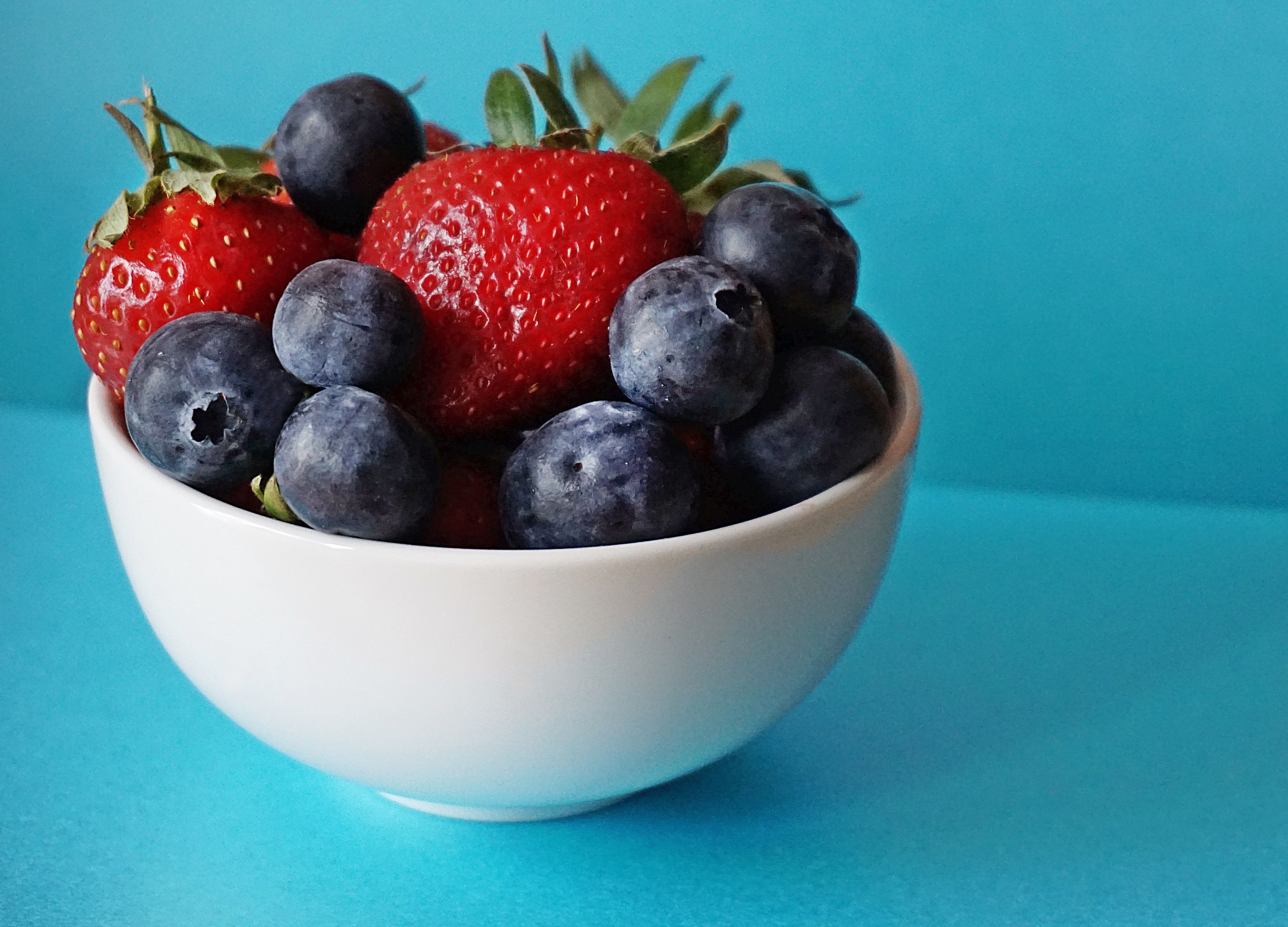 White ceramic bowl filled with fresh ripe strawberries and blueberries against a vivid turquoise background