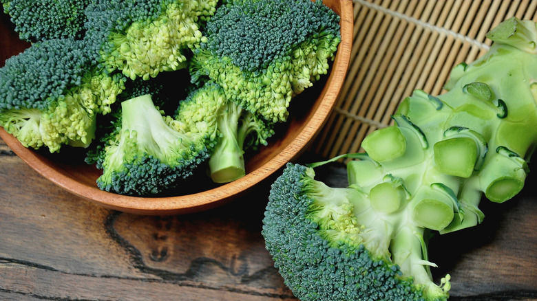 Fresh green broccoli florets in a wooden bowl beside a cut broccoli stalk on a rustic wooden table
