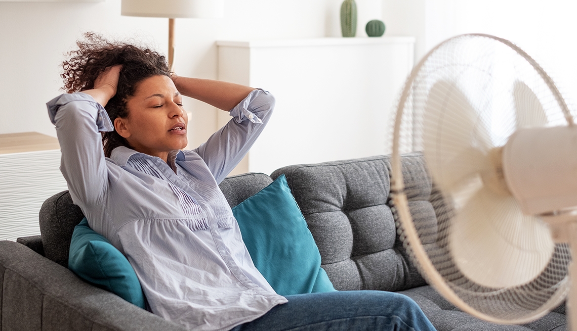 Mulher sentindo calor extremo se refrescando na frente do ventilador no verão