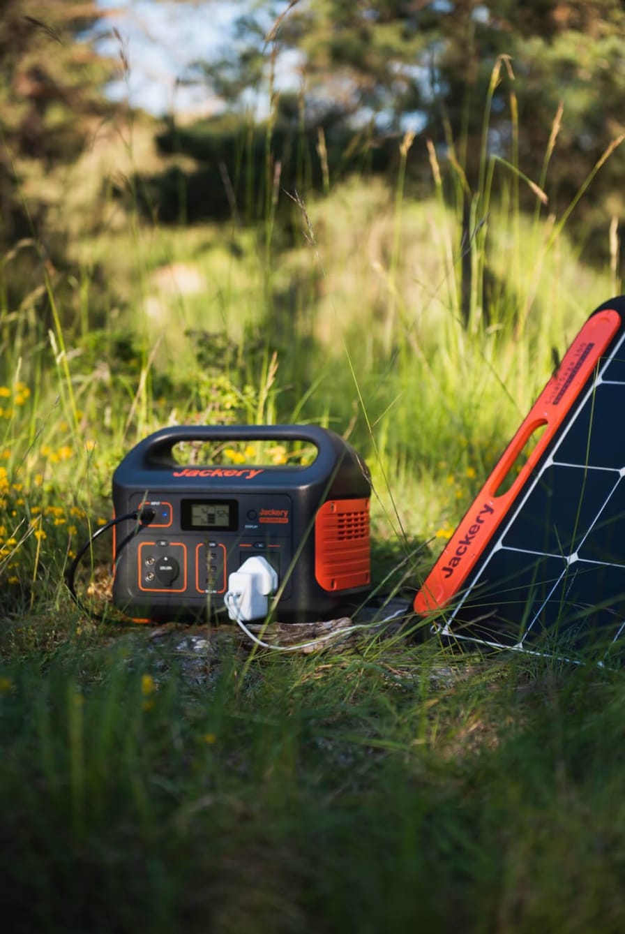 Estação de energia portátil Jackery com painel solar em campo gramado durante camping