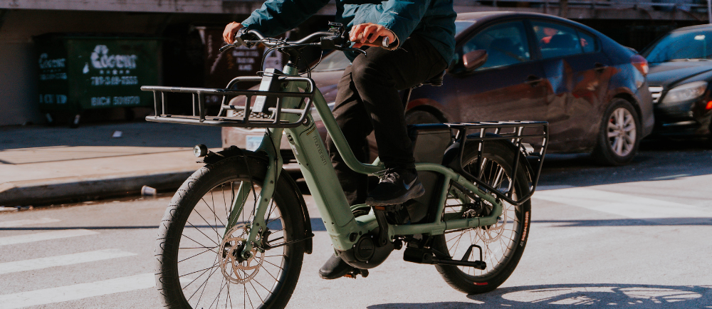 Rider on a green leased e-bike with front and rear racks crossing a city street, a typical e-bike lease Netherlands for employees commuter setup