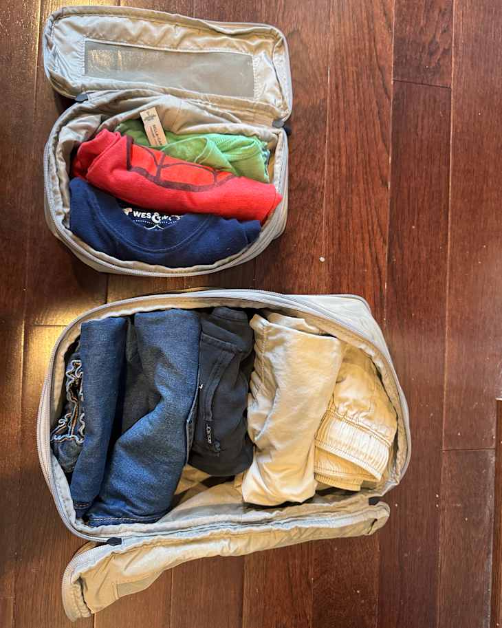 Two packing cubes with rolled clothes on a wooden floor