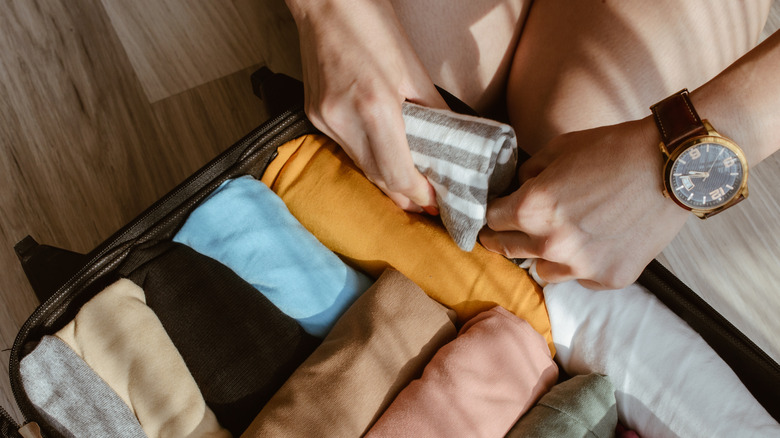 Hands rolling earth-toned clothing tightly into a suitcase