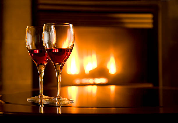Two glasses of red wine glowing in front of a fireplace