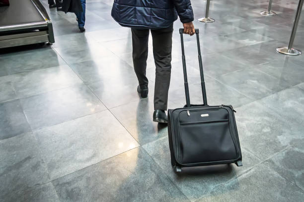 A man walking through an airport terminal pulling a small rolling carry-on