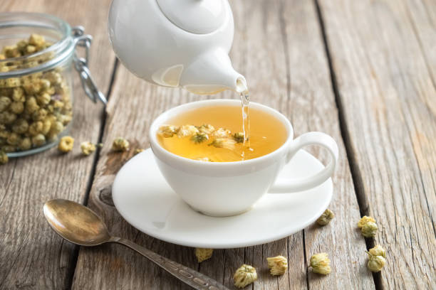 Chamomile tea being poured from a white teapot into a cup