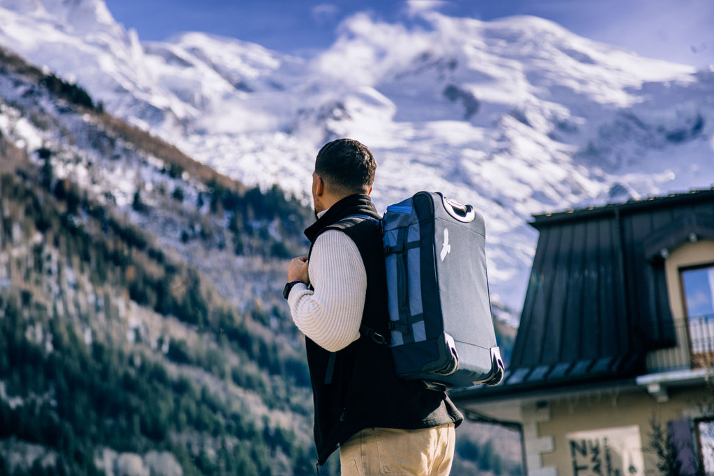 A traveler with a carry-on backpack standing before snowy mountains