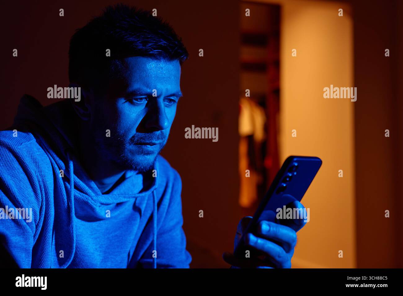 A man’s face lit by the blue light of a smartphone in a dark room