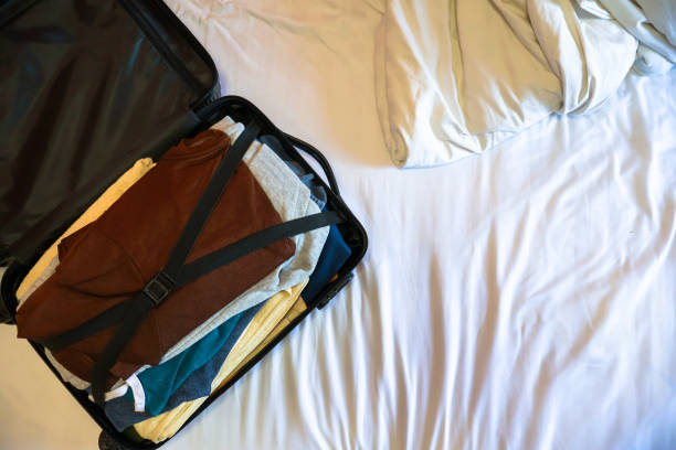 An open carry-on suitcase packed with folded clothes lying on a white bed