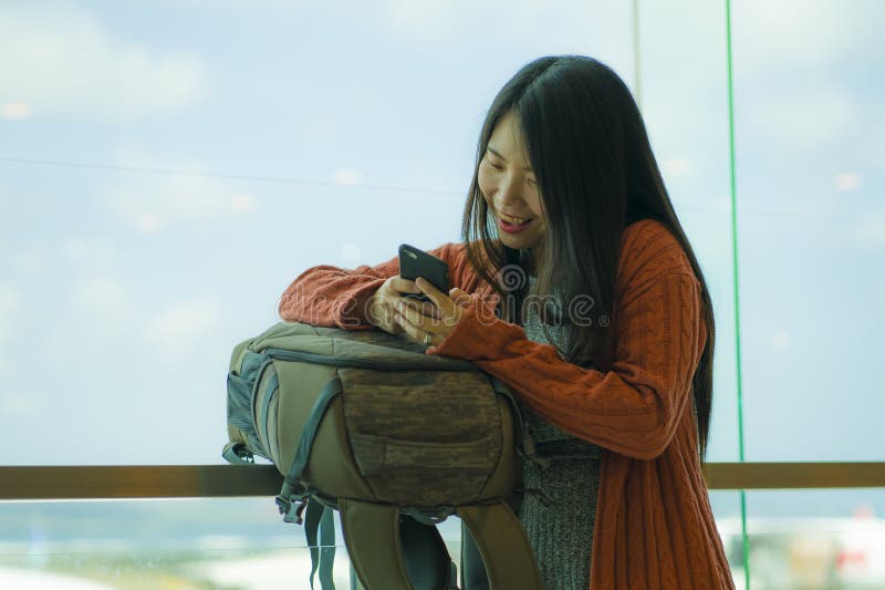 A smiling traveler with a backpack checking her phone at an airport window