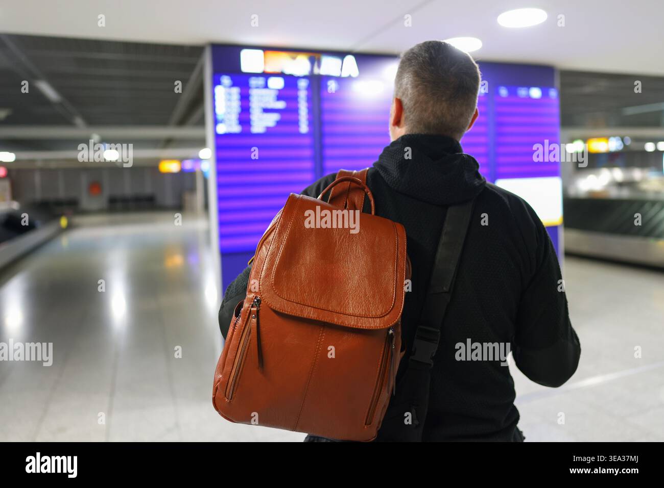A traveler in a hoodie with a backpack checking the departures board