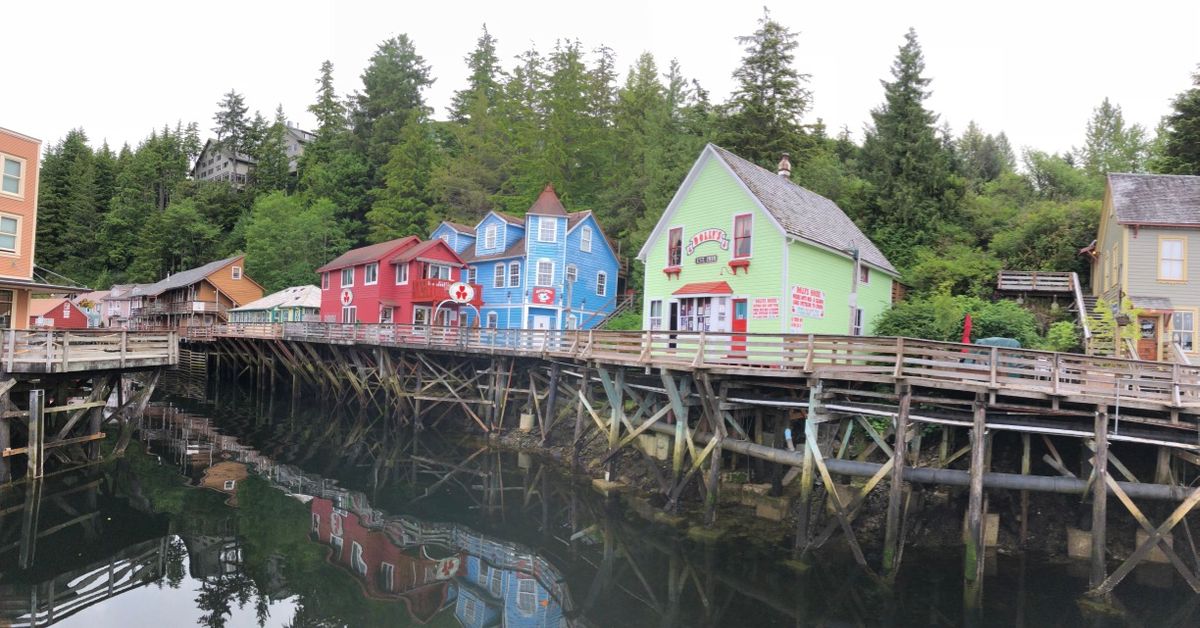 Colorful historic buildings on stilts line Creek Street in Ketchikan, Alaska, reflected in the calm creek below.